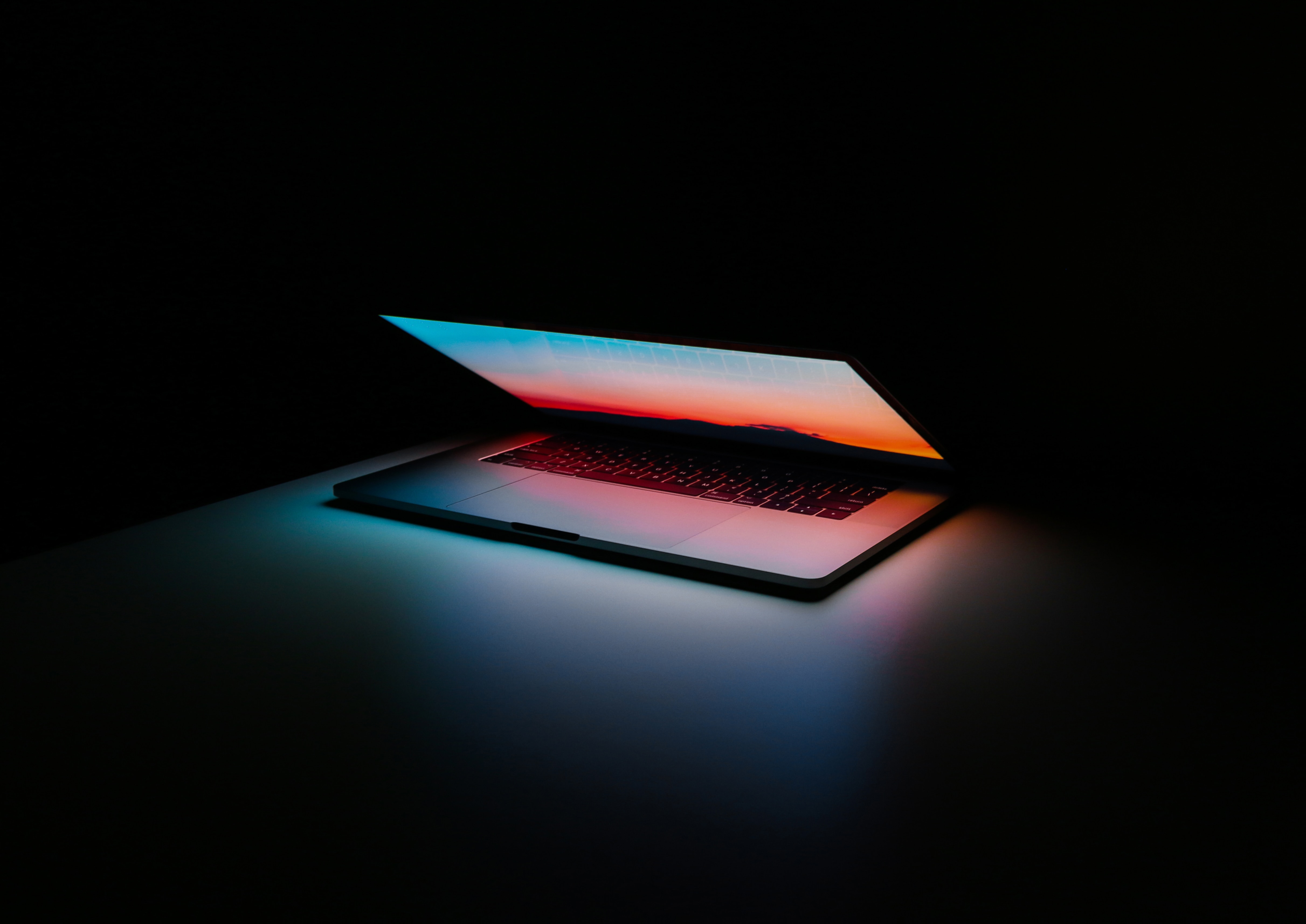 Half-open laptop lying on a table in the dark with its lit up